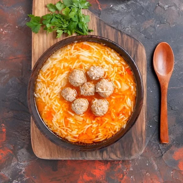 A bowl of Indian curry with meatballs and rice noodles, garnished with fresh parsley.
