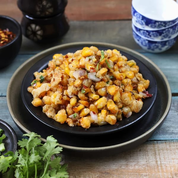 Crispy corn kernels with spices and herbs on a black plate, with cilantro and chili flakes.