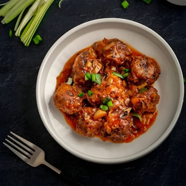 Indian Manchurian dish with meatballs in a rich red sauce, garnished with green onions.