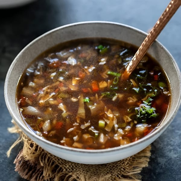 A bowl of Elysian Curry's Indian hot and sour soup with vegetables and a golden spoon.