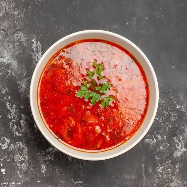 Top-down view of a vibrant red Indian curry in a white bowl, garnished with fresh cilantro.