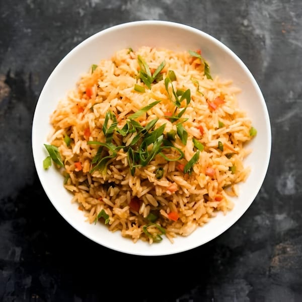 A white bowl filled with Indian fried rice, garnished with chopped green onions, on a dark surface.